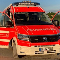 Rotes Feuerwehrfahrzeug, ein Einsatzleitwagen (ELW1), steht mit geöffneten Türen auf einer Betonfläche.