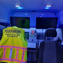 Innenraum eines Feuerwehr-Einsatzfahrzeugs mit Sitzen, Warnweste für Einsatzleiter sowie zwei Computerarbeitsplätze.