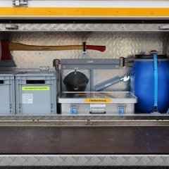Rotes Feuerwehrfahrzeug, ein Gerätewagen Logistik (GW-L 2), geöffneter Gerätekästen der linken Fahrzeugseite mit Beladung.