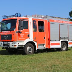 Rotes Feuerwehrfahrzeug, ein Hilfeleistungslöschfahrzeug (HLF 20-16), steht auf einer Rasenfläche.
