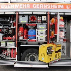 Rotes Feuerwehrfahrzeug, ein Hilfeleistungslöschfahrzeug (HLF 20-16), geöffnete Gerätekästen der linken Fahrzeugseite mit Beladung.