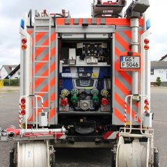 Rotes Feuerwehrfahrzeug, ein Hilfeleistungslöschfahrzeug (HLF 20-16), geöffnete Hecktür mit Beladung.