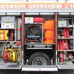 Rotes Feuerwehrfahrzeug, ein Hilfeleistungslöschfahrzeug (HLF 20-16), geöffnete Gerätekästen der rechten Fahrzeugseite mit Beladung.
