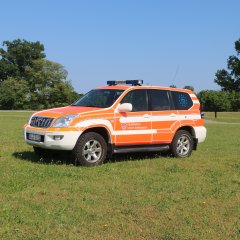 Rotes Feuerwehrfahrzeug, ein Kommandowagen (KdoW), steht auf einer Rasenfläche.