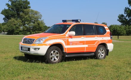Rotes Feuerwehrfahrzeug, ein Kommandowagen (KdoW), steht auf einer Rasenfläche.