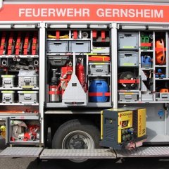 Rotes Feuerwehrfahrzeug, ein Löschfahrzeug (LF 20), mit geöffneten Gerätekästen der rechten Fahrzeugseite mit Beladung.