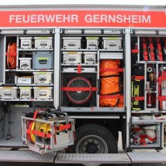 Rotes Feuerwehrfahrzeug, ein Löschfahrzeug (LF 20), mit geöffneten Gerätekästen der linken Fahrzeugseite mit Beladung.