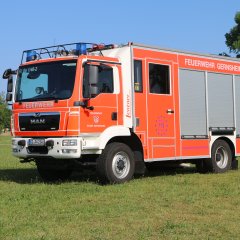 Rotes Feuerwehrfahrzeug, ein Löschfahrzeug (LF 20), steht auf einer Rasenfläche.