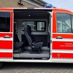 Rotes Feuerwehrfahrzeug, ein Mannschaftstransportwagen (MTW), mit geöffneter Seitentür mit Blick auf die Sitze.
