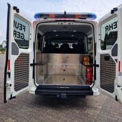 Rotes Feuerwehrfahrzeug, ein Mannschaftstransportwagen (MTW), geöffnete Hecktür mit Blick auf die Sitzplätze.