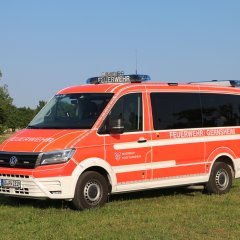 Rotes Feuerwehrfahrzeug, ein Mannschaftstransportwagen (MTW), steht auf einer Rasenfläche.