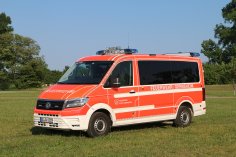 Rotes Feuerwehrfahrzeug, ein Mannschaftstransportwagen (MTW), steht auf einer Rasenfläche.