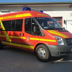 Rotes Feuerwehrfahrzeug, ein Mannschaftstransportwagen (MTW), steht vor einem Feuerwehrgerätehaus.