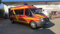 Rotes Feuerwehrfahrzeug, ein Mannschaftstransportwagen (MTW), steht vor einem Feuerwehrgerätehaus.