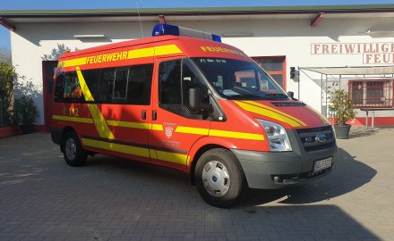 Rotes Feuerwehrfahrzeug, ein Mannschaftstransportwagen (MTW), steht vor einem Feuerwehrgerätehaus.