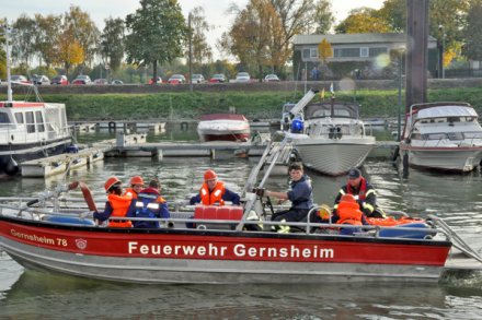 Rotes Feuerwehrboot, ein Mehrzweckboot (MZB), mit sieben Feuerwehrleuten. Das Boot befindet sich in einem Sportboothafen.