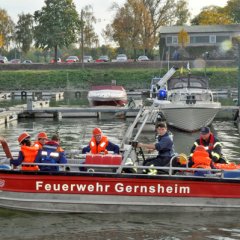 Rotes Feuerwehrboot, ein Mehrzweckboot (MZB), mit sieben Feuerwehrleuten. Das Boot befindet sich in einem Sportboothafen.