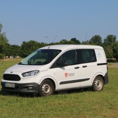 Weißes Feuerwehrfahrzeug, ein PKW, steht auf einer Rasenfläche.