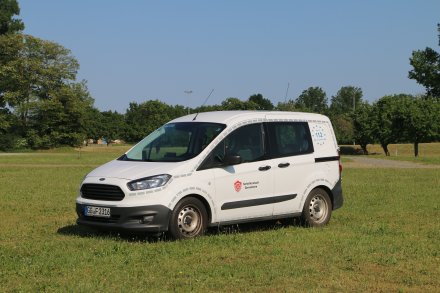 Weißes Feuerwehrfahrzeug, ein PKW, steht auf einer Rasenfläche.