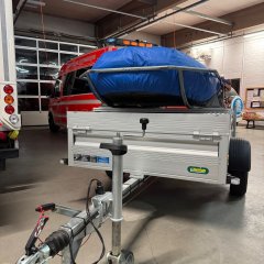 Ein Rettungsboot der Feuerwehr (RTB-1) auf einem silbernen Anhänger. Im Hintergrund die Fahrzeughalle mit verschiedenen Feuerwehrfahrzeugen.