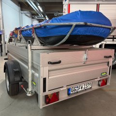 Ein Rettungsboot der Feuerwehr (RTB-1) auf einem silbernen Anhänger. Im Hintergrund die Fahrzeughalle mit verschiedenen Feuerwehrfahrzeugen.