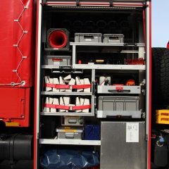 Rotes Feuerwehrfahrzeug, ein Schlauchwagen Katastrophenschutz (SW-KatS), geöffneter Gerätekästen der rechten Fahrzeugseite mit Beladung.