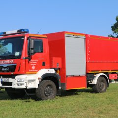 Rotes Feuerwehrfahrzeug, ein Schlauchwagen Katastrophenschutz (SW-KatS), steht auf einer Rasenfläche.