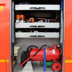 Rotes Feuerwehrfahrzeug, ein Tanklöschfahrzeug (TLF 24/50), geöffneter Gerätekästen der linken Fahrzeugseite mit Beladung.