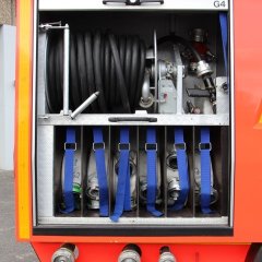 Rotes Feuerwehrfahrzeug, ein Tanklöschfahrzeug (TLF 24/50), geöffneter Gerätekästen der rechten Fahrzeugseite mit Beladung.