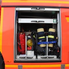 Rotes Feuerwehrfahrzeug, ein Tanklöschfahrzeug (TLF 24/50), geöffneter Gerätekästen der linken Fahrzeugseite mit Beladung.
