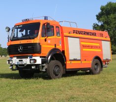 Rotes Feuerwehrfahrzeug, ein Tanklöschfahrzeug (TLF 24/50), steht auf einer Rasenfläche.