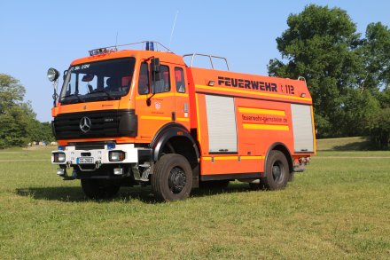 Rotes Feuerwehrfahrzeug, ein Tanklöschfahrzeug (TLF 24/50), steht auf einer Rasenfläche.