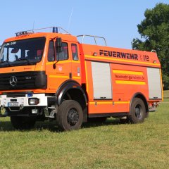 Rotes Feuerwehrfahrzeug, ein Tanklöschfahrzeug (TLF 24/50), steht auf einer Rasenfläche.