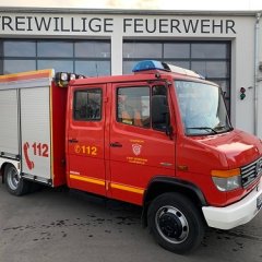 Rotes Feuerwehrfahrzeug, ein Tragkraftspritzenfahrzeug (TSF-W), steht vor einem Feuerwehrgerätehaus.
