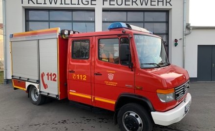 Rotes Feuerwehrfahrzeug, ein Tragkraftspritzenfahrzeug (TSF-W), steht vor einem Feuerwehrgerätehaus.