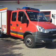 Rotes Feuerwehrfahrzeug, ein Tragkraftspritzenfahrzeug (TSF-W), steht vor einem Feuerwehrgerätehaus.