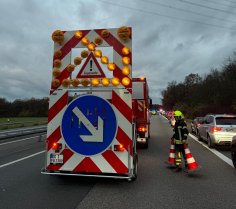 Verkehrssicherungsanhänger an einem Feuerwehrfahrzeug auf der Autobahn. Ein Feuerwehrmann stellt Leitkegel auf.