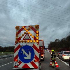 Verkehrssicherungsanhänger an einem Feuerwehrfahrzeug auf der Autobahn. Ein Feuerwehrmann stellt Leitkegel auf.