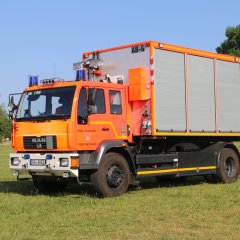 Rotes Feuerwehrfahrzeug, ein Wechselladerfahrzeug (WLF), steht auf einer Rasenfläche.