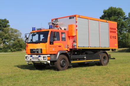 Rotes Feuerwehrfahrzeug, ein Wechselladerfahrzeug (WLF), steht auf einer Rasenfläche.