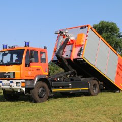 Rotes Feuerwehrfahrzeug, ein Wechselladerfahrzeug (WLF), steht auf einer Rasenfläche.