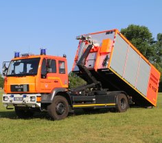 Rotes Feuerwehrfahrzeug, ein Wechselladerfahrzeug (WLF), steht auf einer Rasenfläche.