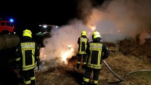 Drei Einsatzkräfte der Feiwilligen Feuerwehr Gernsheim löschen bei einem nächtlichen Einsatz einen Heuhaufen. Rauch steigt aus der Mitte des Bilds auf. Man sieht kleine Flammen am Boden.